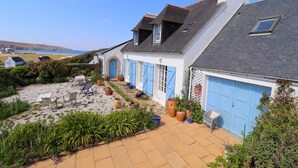Una casa costera con un patio, mobiliario exterior y vista al mar.