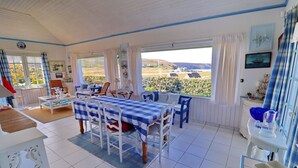 Una habitación iluminada por el sol, con una mesa a cuadros, sillas y vistas al campo.