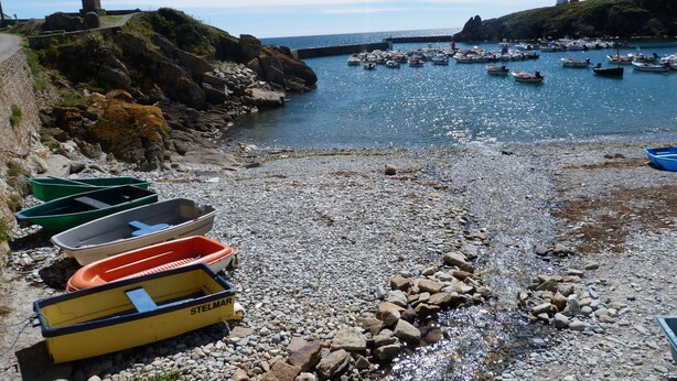 A rocky beach with boats and a lighthouse in the background.