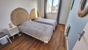 A bedroom with two beds, a bedside table, a radiator, and a window with a view of buildings.