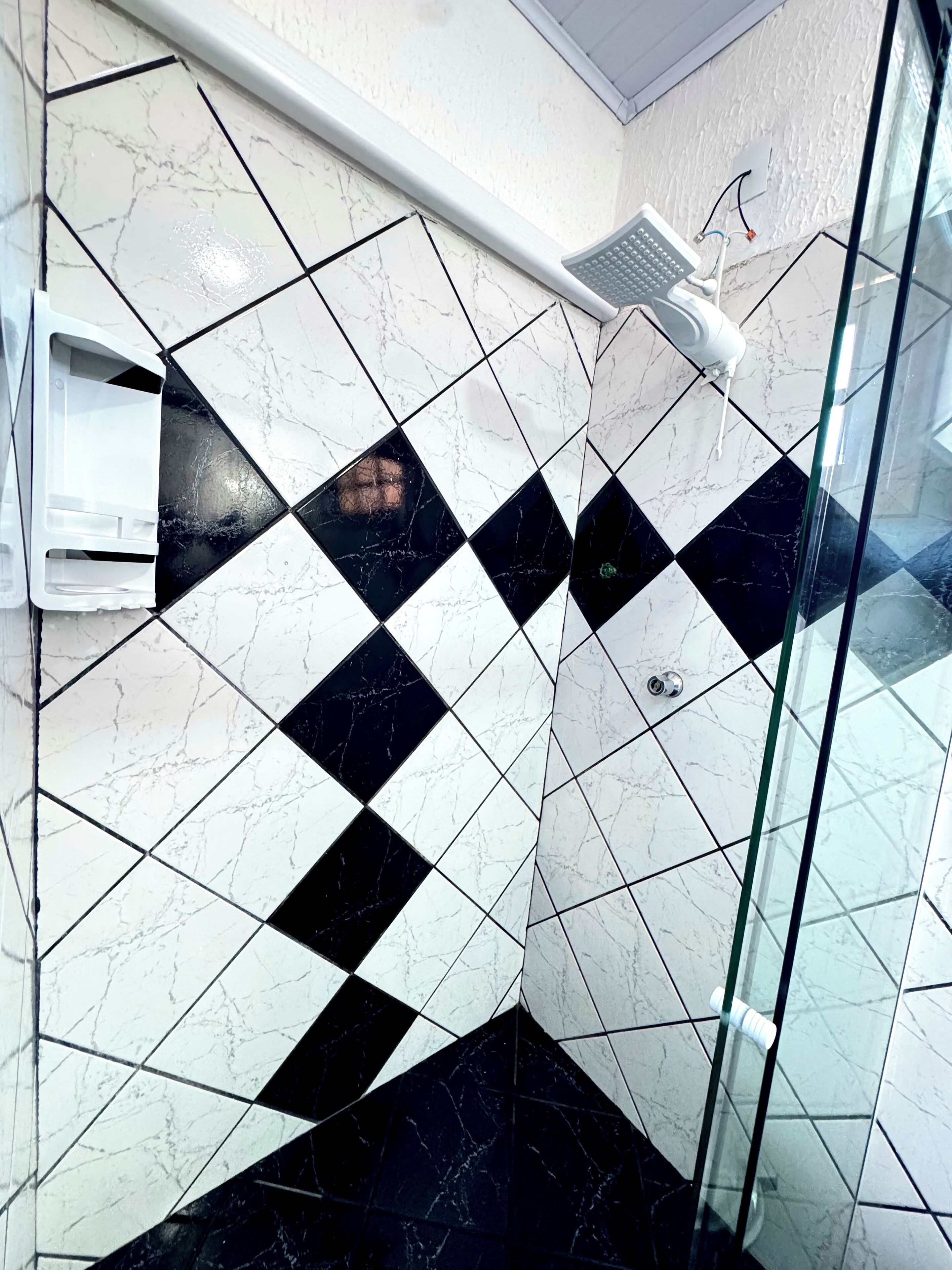 A bathroom with a checkered black and white tile pattern, a glass shower enclosure, and a white towel dispenser.