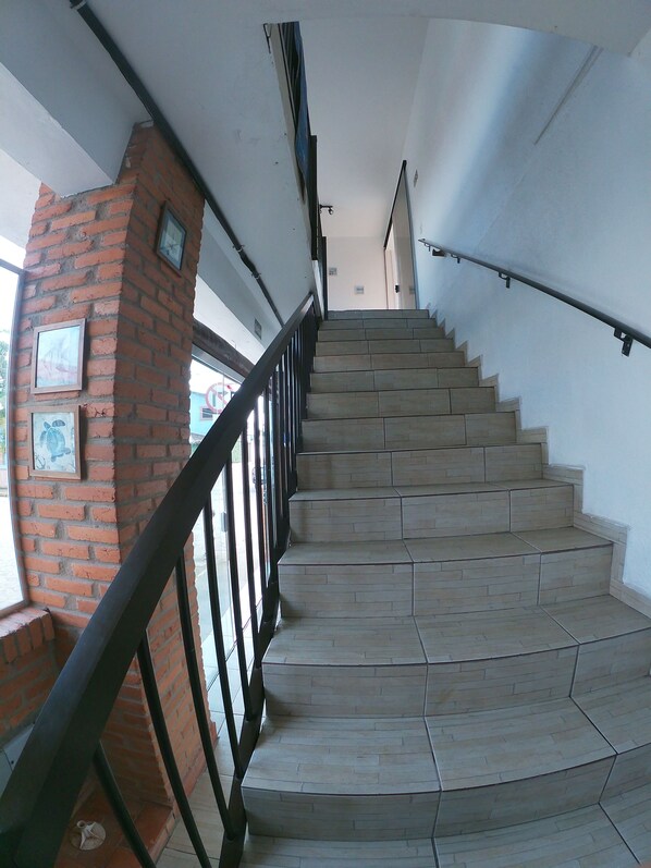 Una escalera con un pilar de ladrillo y barandilla de metal, que sube a un nivel superior.