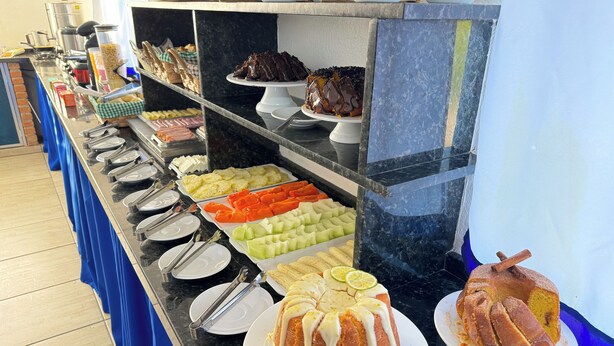 Un bufé con diversos alimentos, incluyendo frutas, pasteles y un pastel con cobertura blanca y rebanadas de limón.