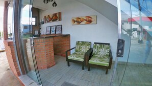 Un área de recepción con puerta de cristal, dos sillones tapizados con motivos florales, un pilar de ladrillo y obras de arte en la pared.
