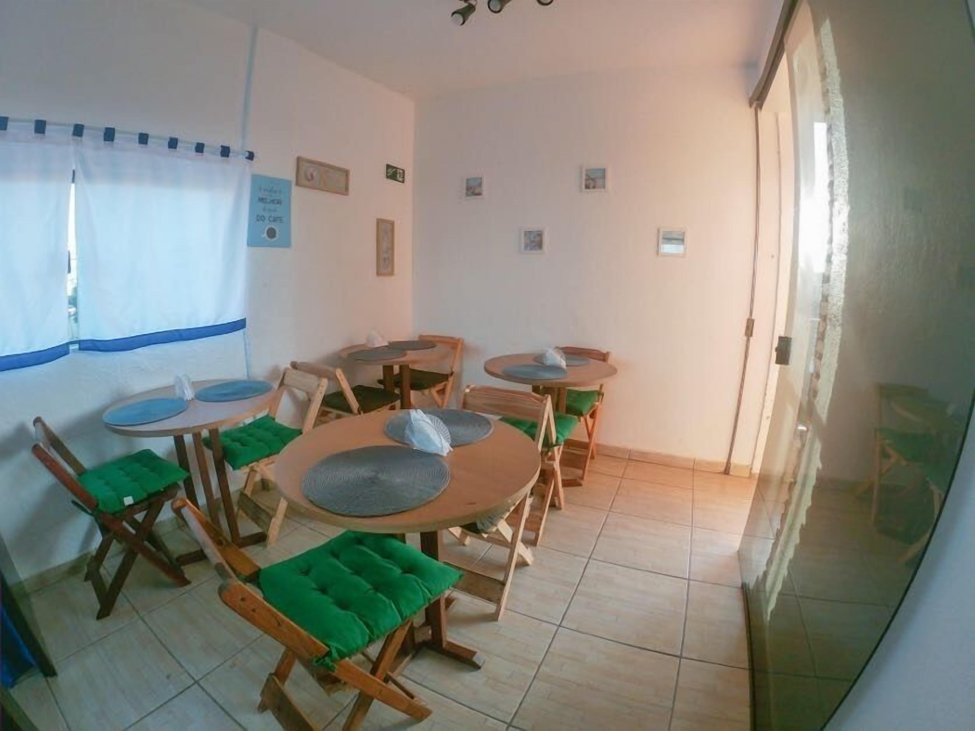 A dining area with wooden tables and chairs, a window with a blue curtain, and a door leading outside.