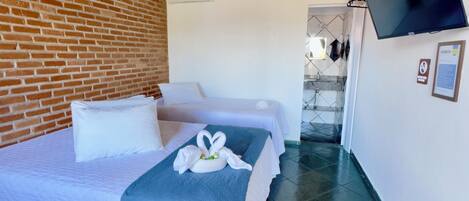 Habitación de hotel con pared de ladrillo, cama con ropa de cama blanca, manta azul y almohada con forma de cisne.