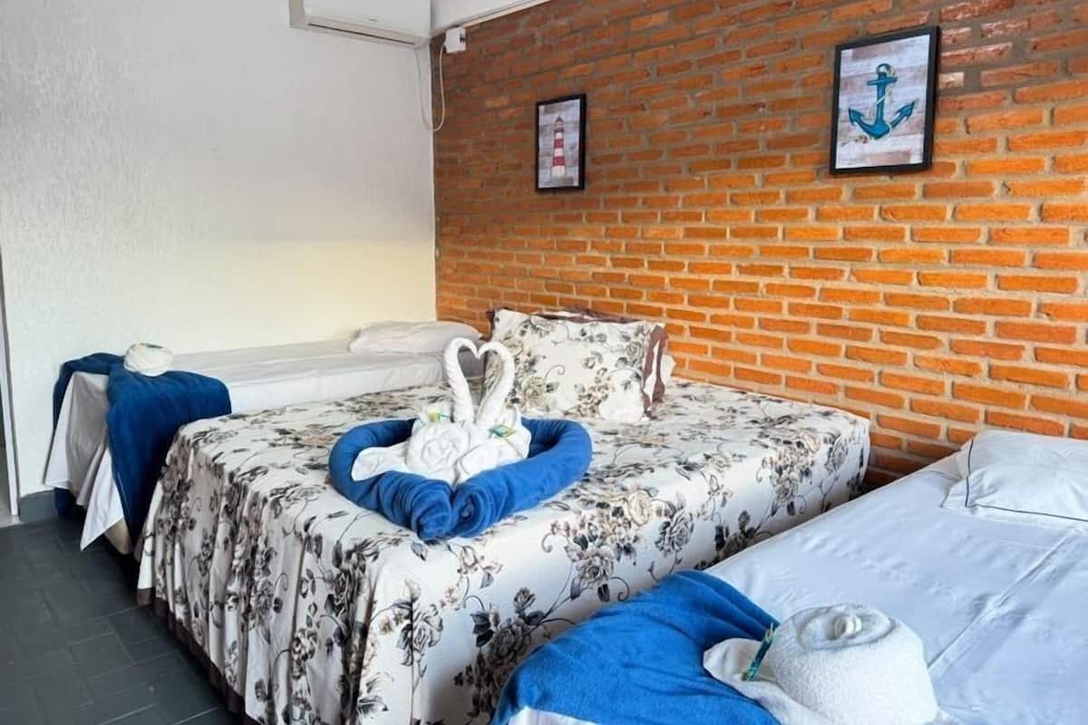 Habitación de hotel con pared de ladrillo, cama con ropa de cama floral, otra cama, una toalla azul y una toalla blanca.