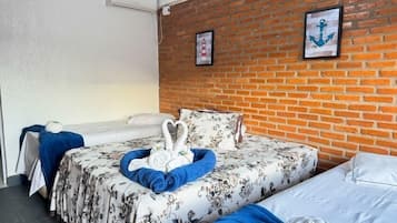 Habitación de hotel con pared de ladrillo, cama con ropa de cama floral, otra cama, una toalla azul y una toalla blanca.