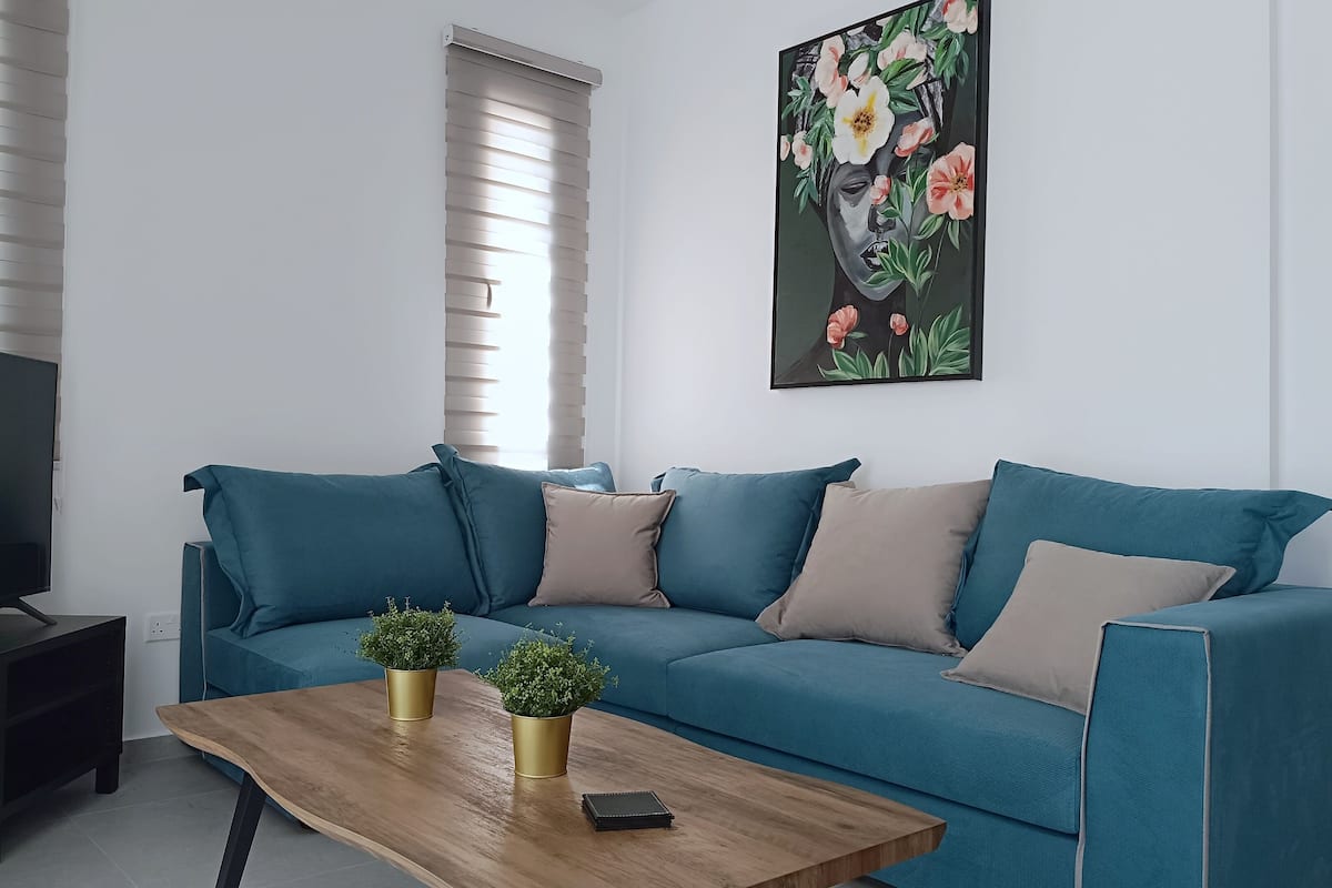 Una sala de estar moderna con un sofá azul turquesa, una mesa de centro de madera y un televisor sobre un mueble.