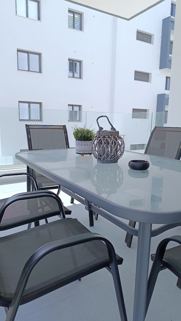 A glass-top table with four chairs, a potted plant, and a decorative item on a balcony. - Larvella Estia Luxury Suites (Larnaca)
