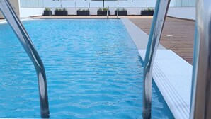 A swimming pool with metal ladders, surrounded by a wooden deck and potted plants. - Larvella Estia Luxury Suites (Larnaca)
