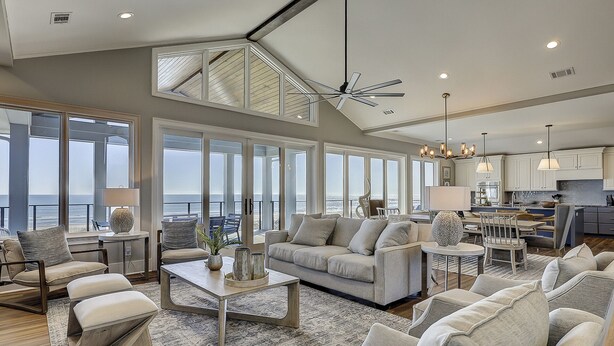 A spacious living area with a large sofa, a coffee table, and a view of the ocean through large windows. - 11 Sea Hawk Lane - Oceanfront Oasis: Stylish Coastal Living & Endless Views (Hilton Head Island)