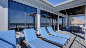 A sun deck with lounge chairs, large windows, and a view of the beach. - 11 Sea Hawk Lane - Oceanfront Oasis: Stylish Coastal Living & Endless Views (Hilton Head Island)