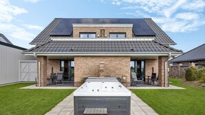 Ein zweistöckiges Haus mit einer Terrassenfläche, einem Whirlpool und Solaranlagen auf dem Dach.
