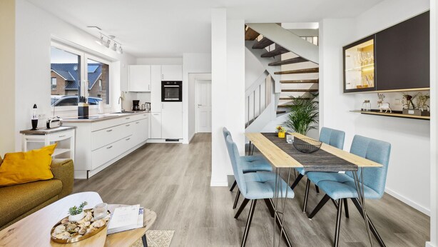 Eine moderne Küche mit weißen Schränken, einem eingebauten Backofen und einem Essbereich mit Holztisch und blauen Stühlen.