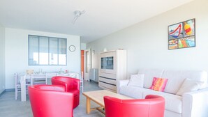 Un salon moderne avec un canapé blanc, des fauteuils rouges, une table basse en bois et un coin repas comprenant une table et des chaises blanches.