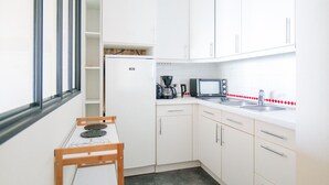 Une petite cuisine équipée avec des meubles blancs, un four à micro-ondes, une machine à café et une petite table avec une chaise.