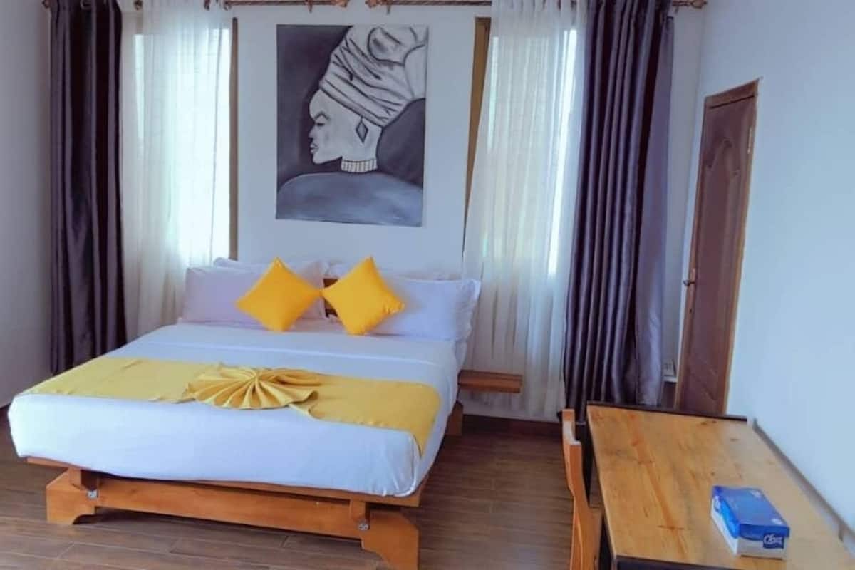 A bedroom with a bed, two pillows, a wooden table, and a painting on the wall.