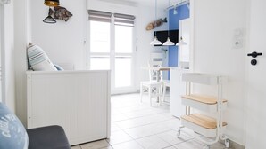 A modern, well-lit room with a white door, a dining area with white chairs and a table, and a white shelf unit with wooden shelves.
