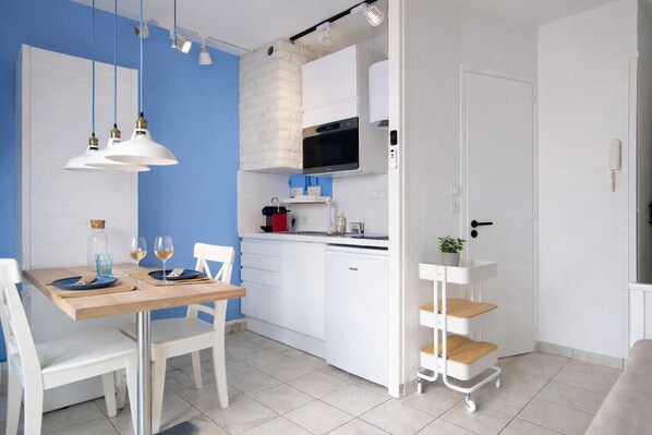 A compact kitchen with white cabinets, a microwave, and a small countertop. There is a dining table with chairs and a hanging light fixture. - Nice renovated studio in Port Olona Les Sables for 2 people (Les Sables-d´Olonne)