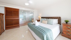 Quarto com cama grande, guarda-roupa de madeira, mesa de cabeceira e planta em vaso.