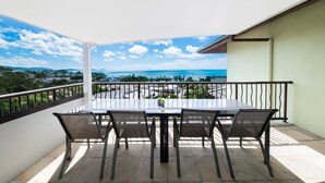 Uma varanda com mesa e cadeiras, vista para o mar, e um corrimão.