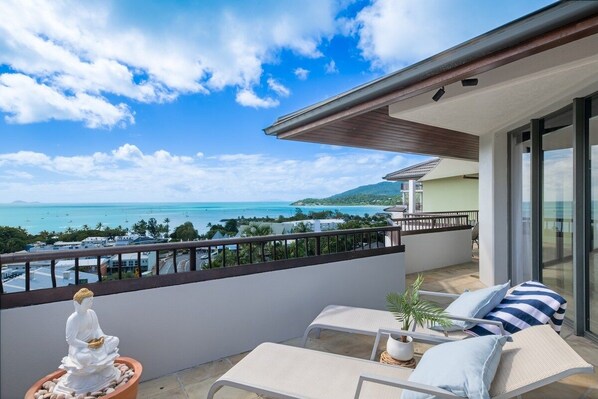 Un balcon avec vue sur la mer, une statue de Bouddha et deux fauteuils de relaxation.