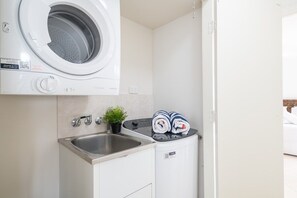 Un área de lavandería compacta con lavadora, lavamanos y un mueble pequeño.