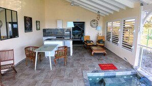 A spacious living area with a kitchen, dining table, chairs, a small seating area with a sofa, and a hot tub. - Magnifique Loft Avec vue Imprenable sur la mer (Grand-Bourg)