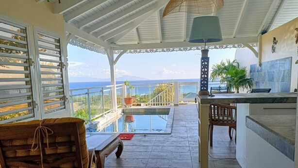 A covered outdoor area with a pool, a wooden chair, a table, and a view of the sea. - Magnifique Loft Avec vue Imprenable sur la mer (Grand-Bourg)