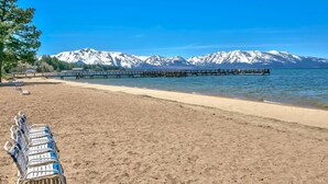Una platja amb un moll de fusta que s'endinsa en aigües tranquil·les, envoltada per muntanyes nevades.