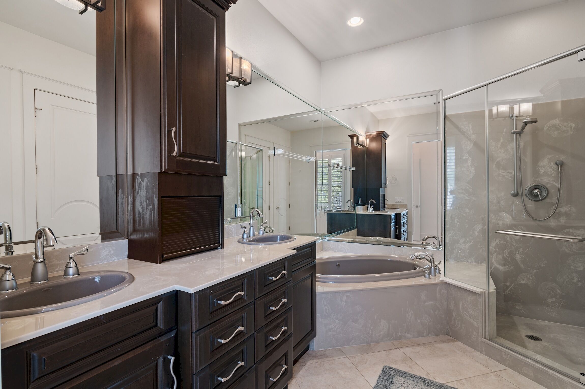 Une salle de bain moderne avec des meubles en bois foncé, un meuble-lavabo à deux vasques, une grande baignoire sur pieds et une douche séparée par des parois en verre.