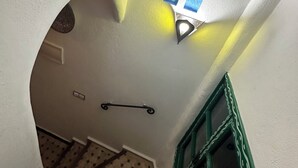 En trappe med et mønstret gulv, et vindue med grøn ramme og en vægmonteret lampe.