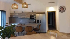 Una cuina moderna amb bigues de fusta, llums penjants i una zona de menjador amb taula i cadires.