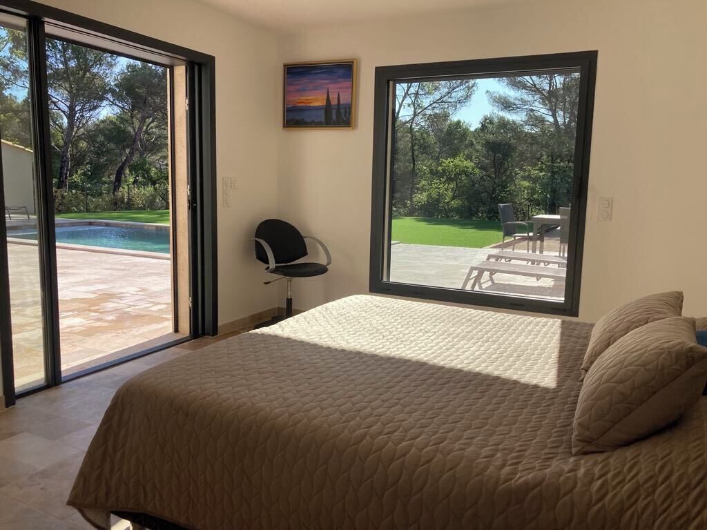 A bedroom with a large bed, a chair, and a view of a swimming pool and garden through a sliding glass door.