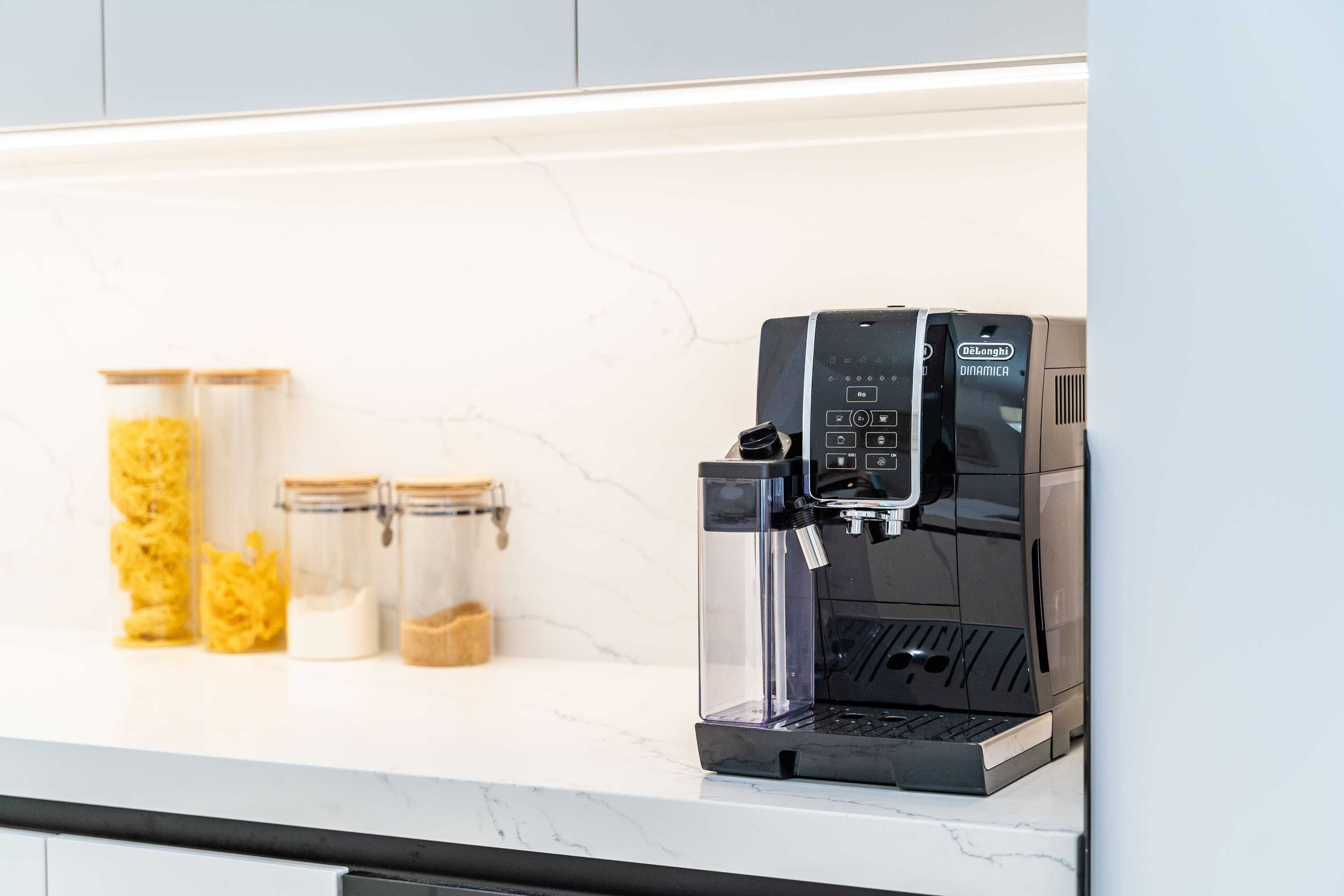 En kaffemaskin placerad på en vit bänkskiva med en väggbeklädnad av marmor bakom.