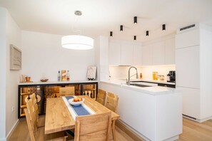 A modern kitchen with white cabinetry, a wooden dining table with chairs, and a central island with a sink.