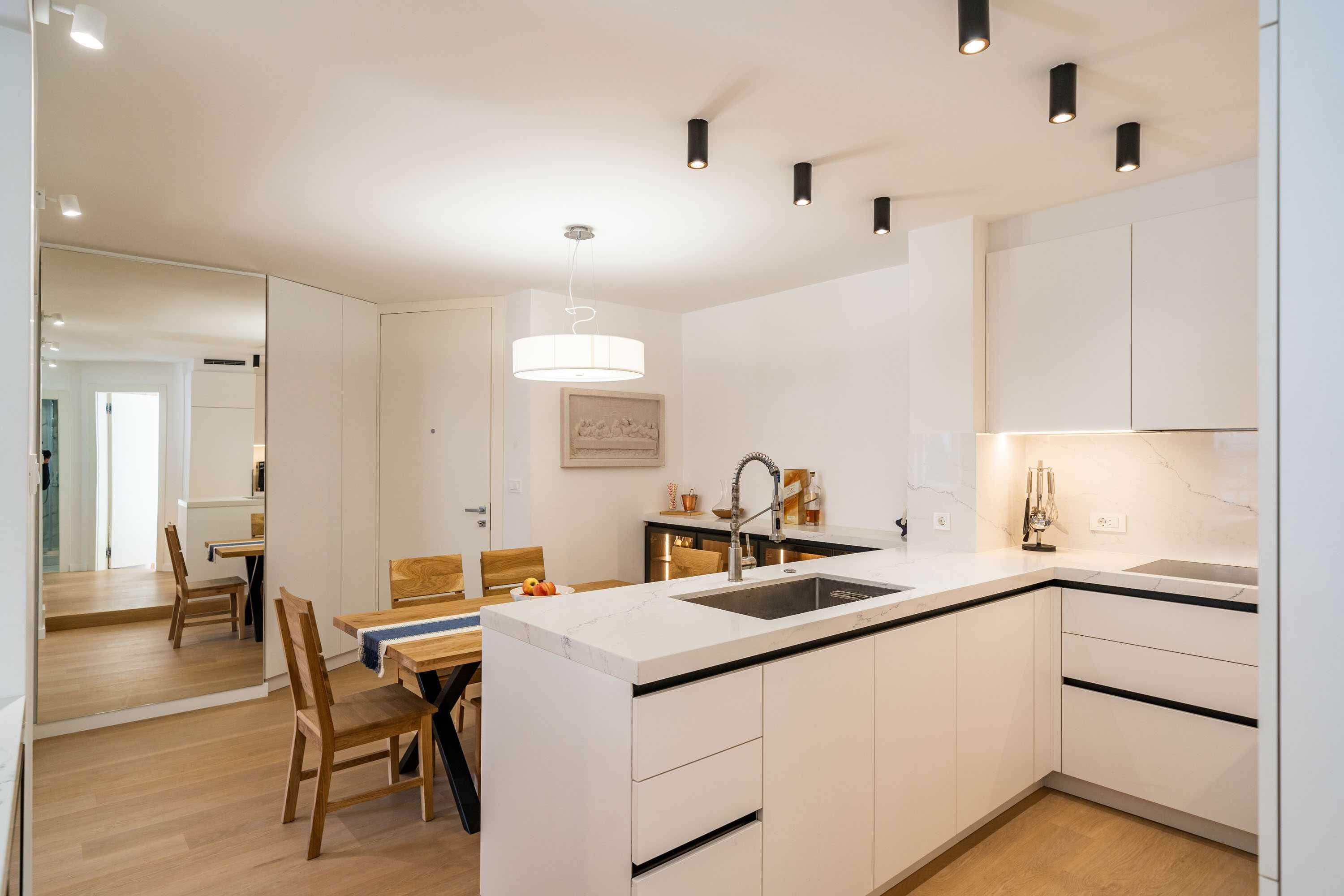 A modern kitchen with white cabinetry, a central island with a sink, and a dining area with wooden chairs and a table.