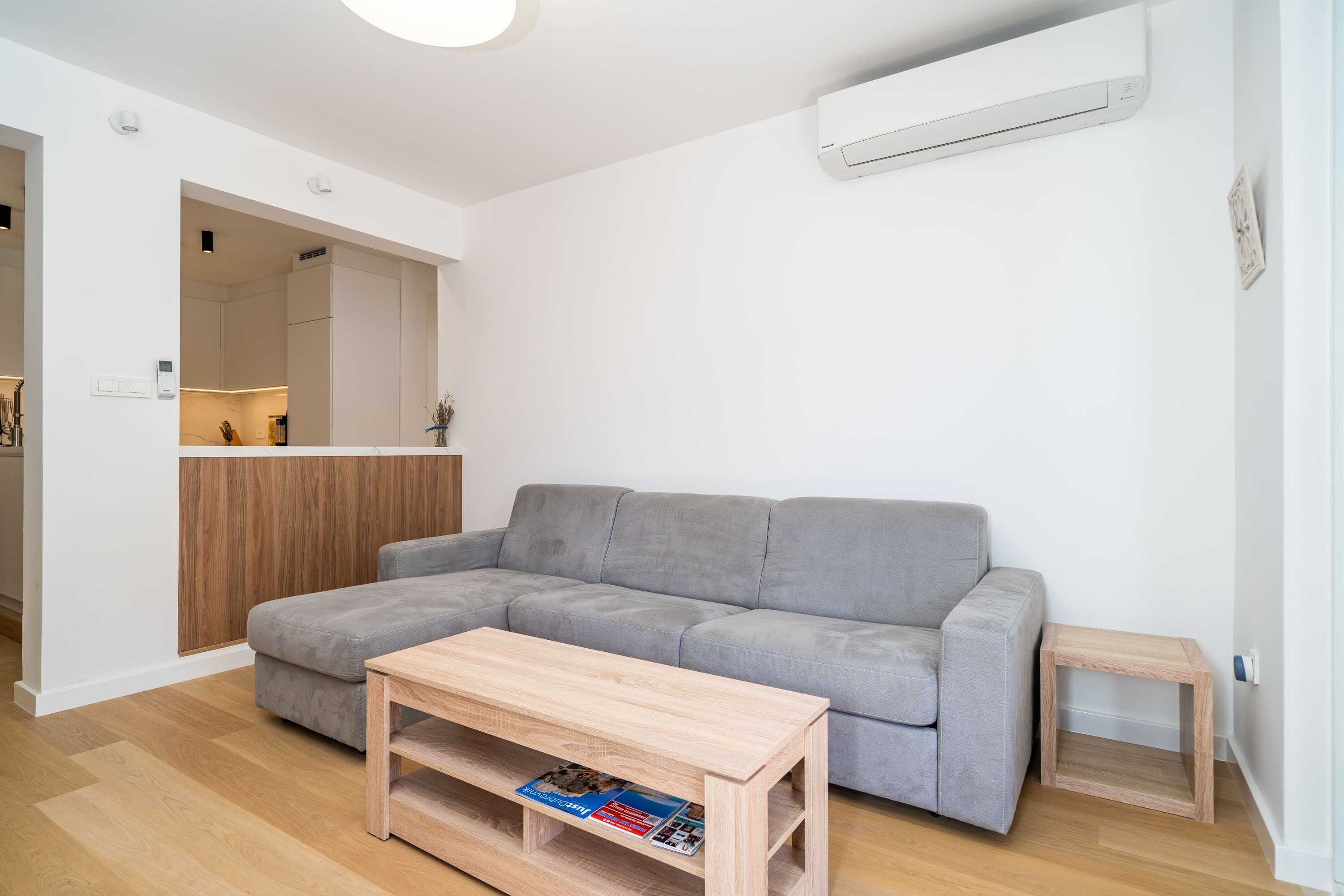 A modern living room with a grey sofa, a wooden coffee table, and a small wooden side table.
