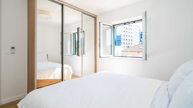 Ein modernes Schlafzimmer mit einem großen Bett, einer Schiebetür zu einem Balkon und einem Fenster mit Blick auf die Stadt.