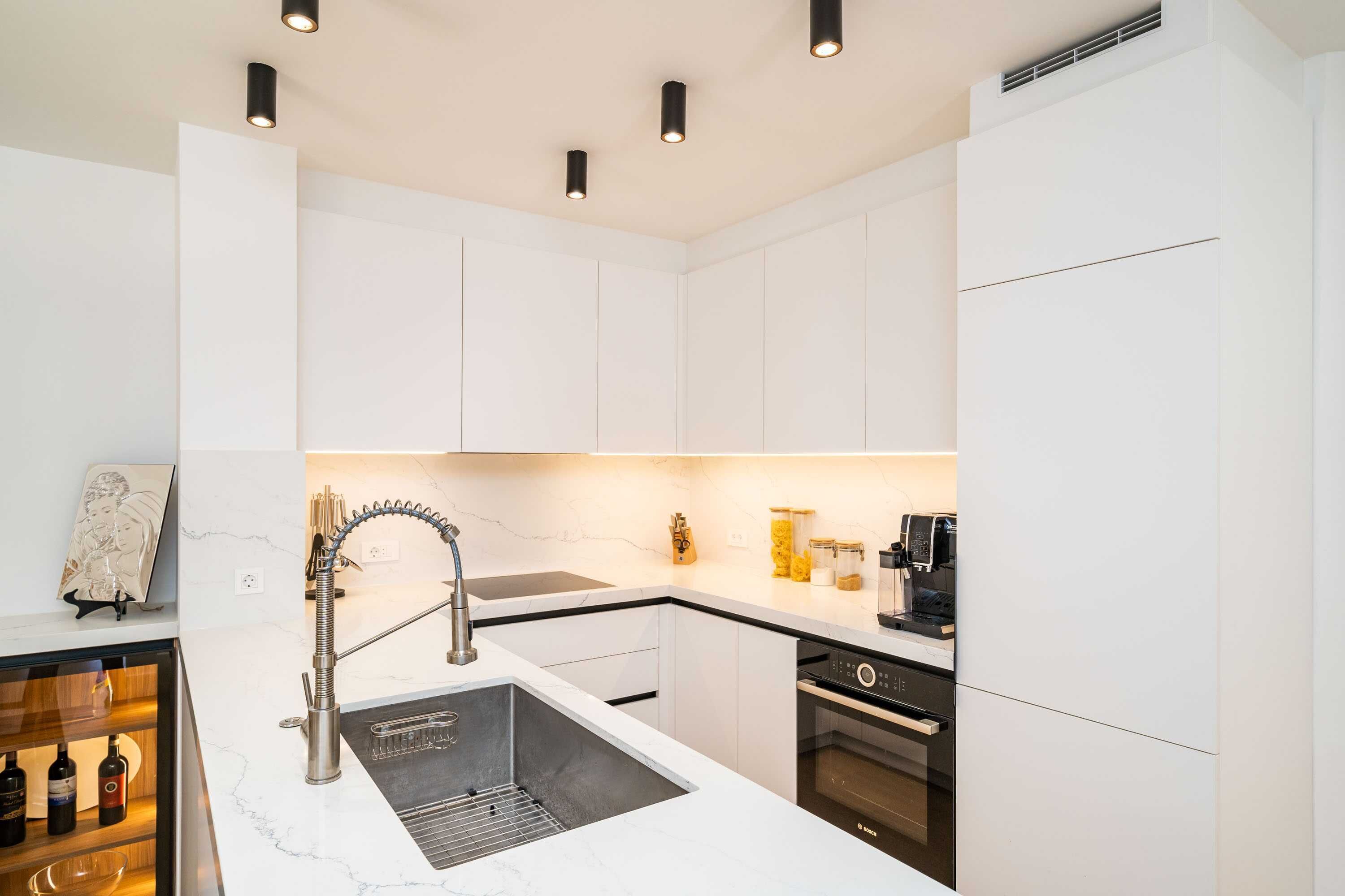 Eine moderne Küche mit weißen Schränken, einer Edelstahlspüle und einem Backofen von Bosch.
