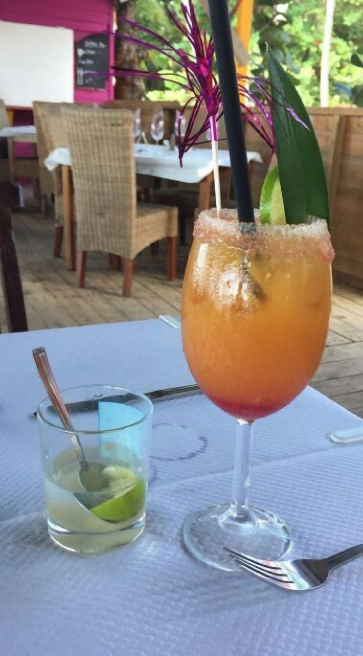 A table with a drink in a glass, a small glass with a lime, and cutlery.