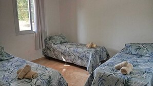Una stanza con tre letti singoli, ognuno con copriletto a motivo di foglia di bambù e asciugamani arrotolati sopra.