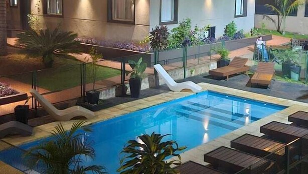 Un hotel con piscina, area salotto esterna e facciata luminosa.