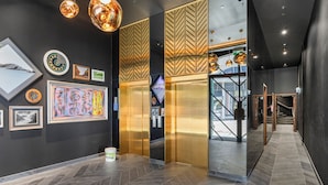 Eine moderne Lobby mit einem Fischgrätparkett, einem zentralen Aufzug und Kunstwerken an den Wänden.