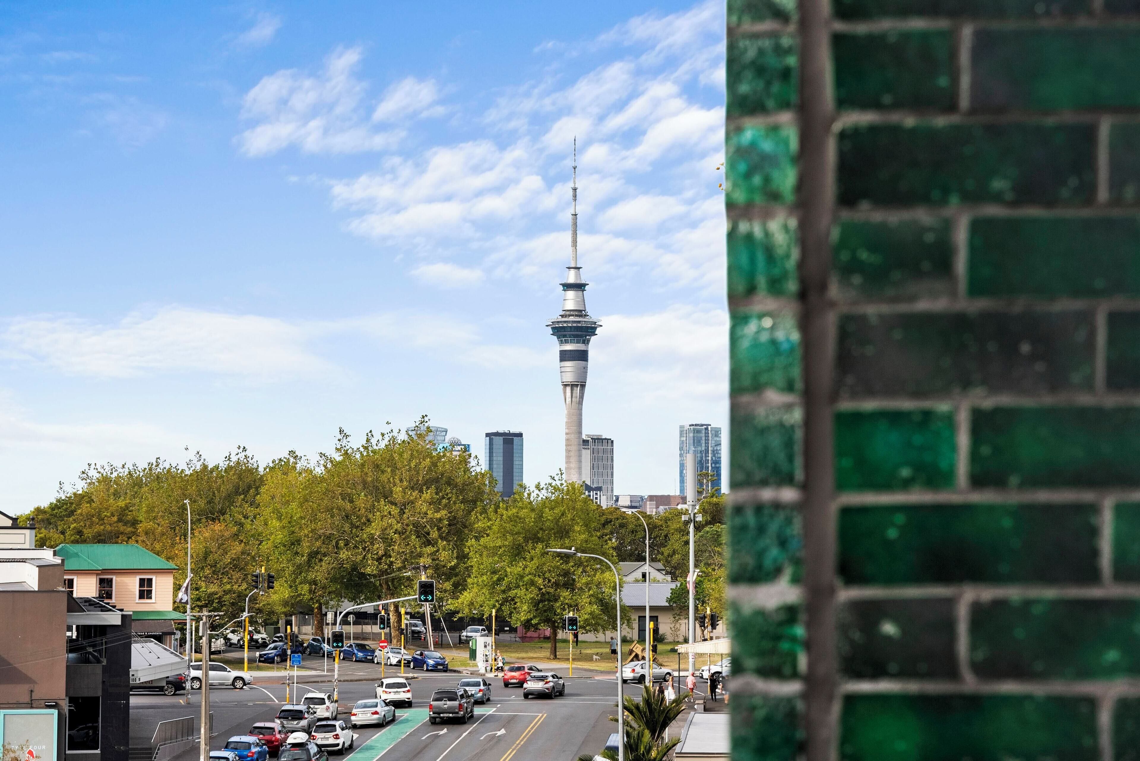 Un paisaje urbano con una torre destacada, un cruce concurrido y un muro de ladrillo verde.