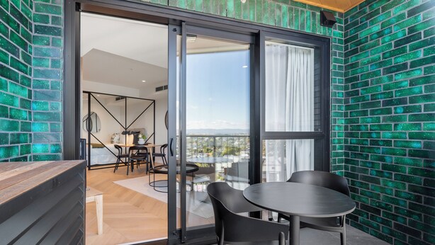 Ein modernes Zimmer mit einer Schiebeglastür, die zu einem Balkon mit Blick auf die Stadt führt.