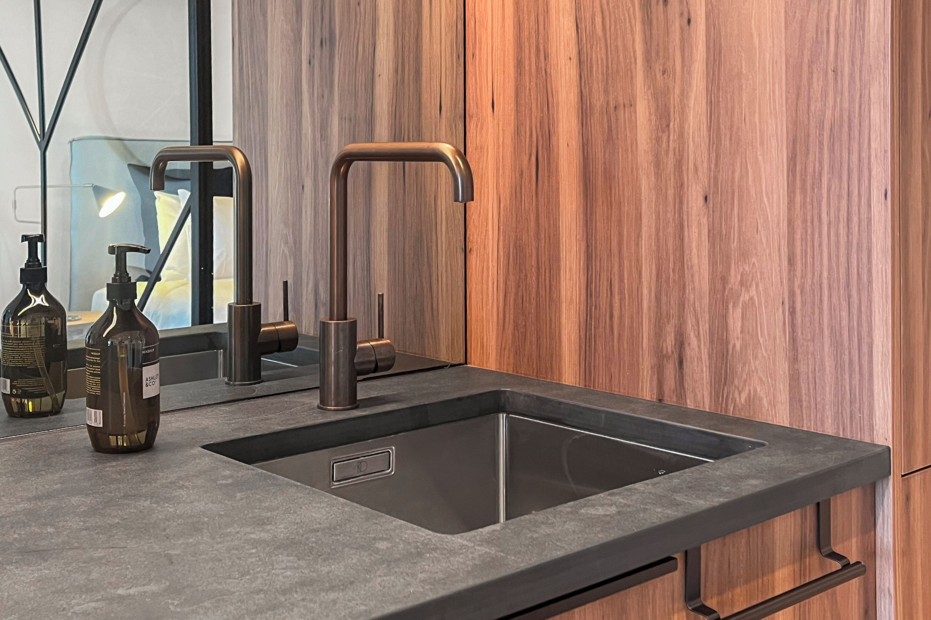 A modern kitchen with a sleek black sink, stainless steel faucet, and a wooden wall.