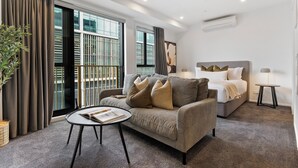 Ein modernes Hotelzimmer mit einer Couch, einem runden Tisch, einem Bett und einem großen Fenster mit Vorhängen.