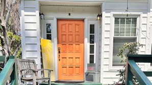 A wooden porch with green steps leading to a white house with a bright orange door. - Family Hideaway ,family friendly and pet friendly. (Virginia Beach)